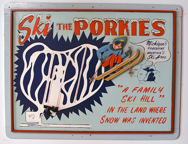 A vintage wooden sign displays an ad for skiing at the Porcupine Mountains.