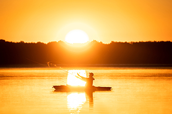 An angler casts a line from his boat while the sun sets over the water at Interlochen State Park in Grand Traverse County.