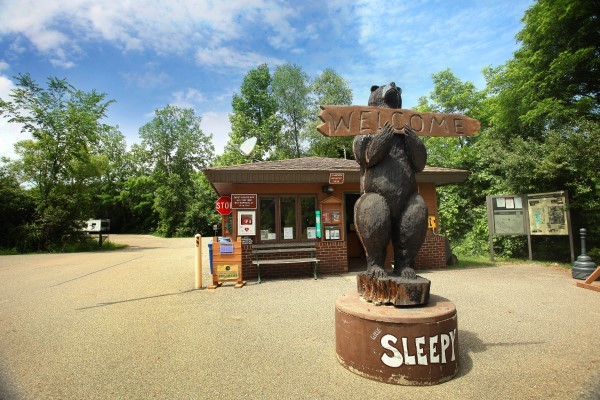 The entrance of Sleepy Hollow State Park, which features a wooden bear statue holiding a "Welcome" sign.
