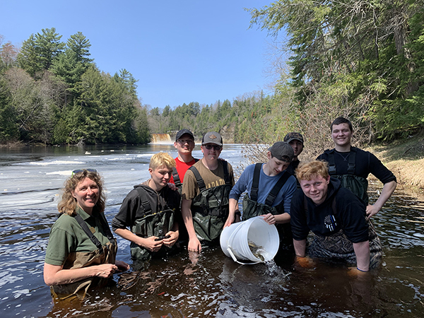 group of students in waders in river stocking fish from a bucket