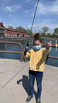 Young girl in face mask holding up fishing rod with perch on it