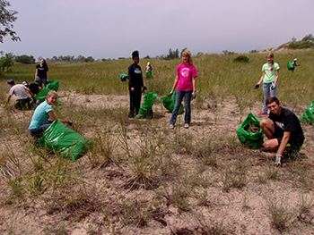 group of young volunteers holding trash bags in a sandy dune area