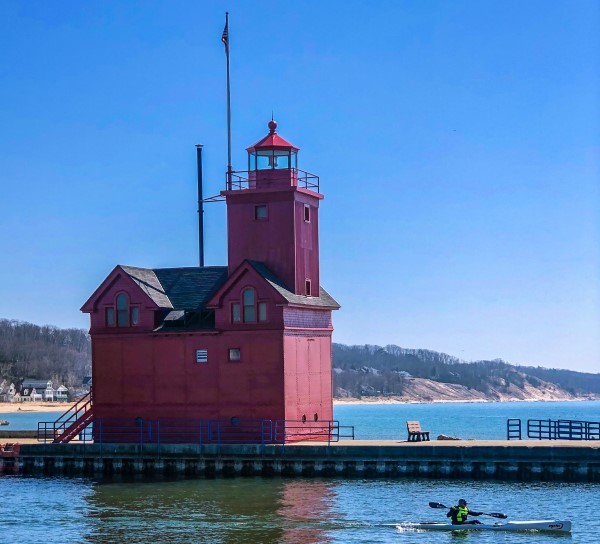 A kayaker paddles past a bright red lighthouse.
