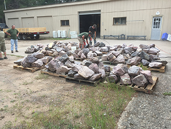 DNR staffers work with a pile of boulders outside a storage buildling