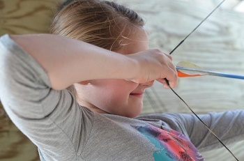 A young child pulls the drawstring of a knocked arrow.