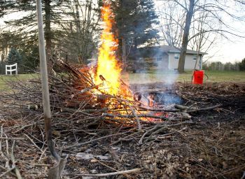 A closeup of a properly built debris fire, including flames, space around the fire and a bucket of water nearby and a shovel. 