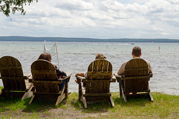 three people sitting in wooden chairs on shore of Higgins Lake