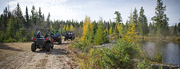 three ORVs riding on trail with lake off to the side