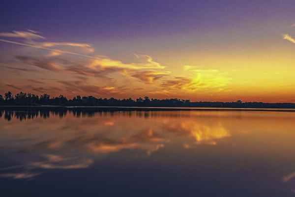 A place lake reflects beautiful, gold and orange whispy clouds at sunset. 