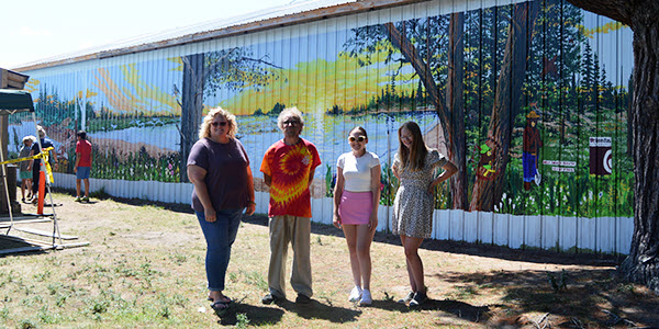 An education coordinator, professional muralist and two students stand in front of the mural at the DNR Pocket Park.