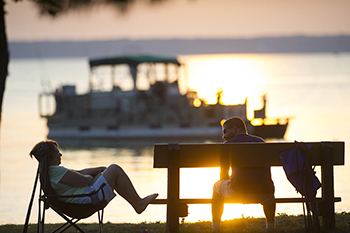 visitor sitting on bench talking with woman in chair along water