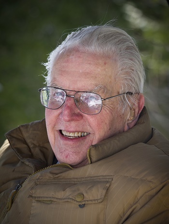 Dr. Tanner, an elderly man with pale skin and large glasses, smiles directly at the camera.