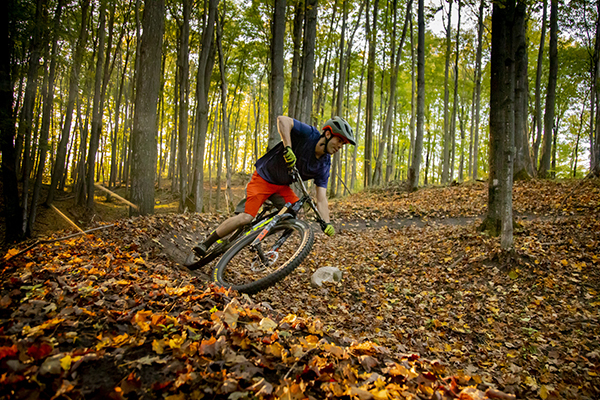 man riding mountain bike on wooded trail with colorful fall leaves on the ground