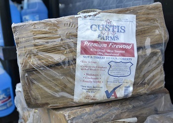 A shrink-wrapped bundle of firewood with a paper label beneath the plastic. The label bears the USDA shield indicated it is certified wood.