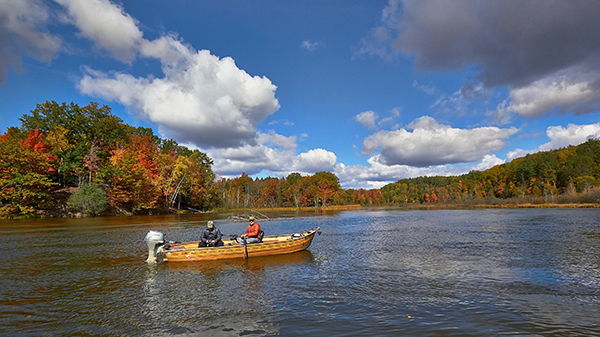 two men in fishing boat on lake surrounded by fall foliage