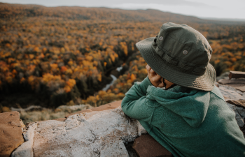A small child gazes out across a forested valley with a river cutting through the tapestry of fall color. 