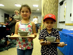 Two young children show off clay pinch pots.