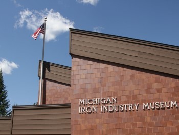 The Michigan Iron Industry Museum, a red brick and sharlply slanted brown-roofed building.