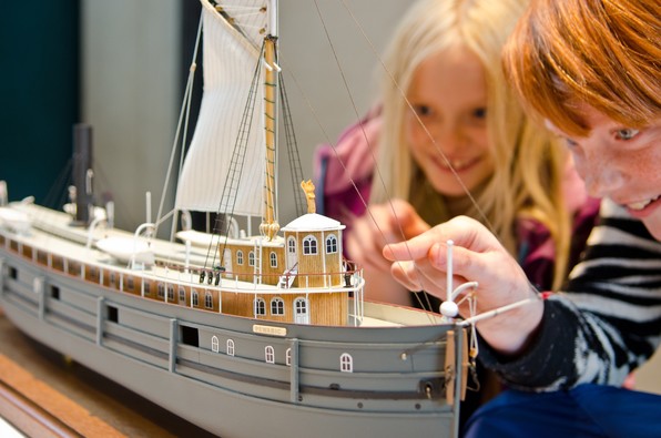 Two children inspect a model of the ship Pewabic. Both are smiling and are looking intently at the details of the model.