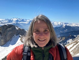 Wildlife biologist Kristie Sitar with snow covered mountains and clear blue sky in the background.