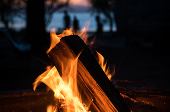 campfire with the silhouettes of campers walking along lakeshore