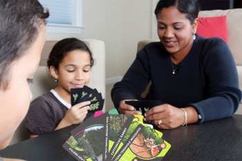 A family sits merrily at a dinner table playing What in the Wild, the DNR's card game.
