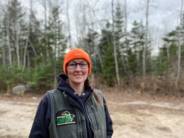 Wildlife technician Jayne Roohr stands in a forest opening wearing an orange hat and DNR vest.