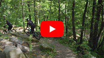 Screenshot of two mountain bikers on trail with play button