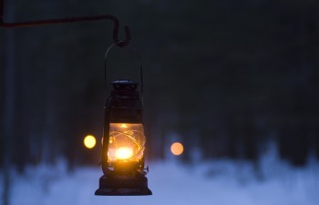 A vintage-style hurricane lantern hangs from a hook at dusk in winter.