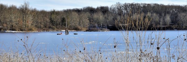 Two adult anglers walk across an iced-over lake.