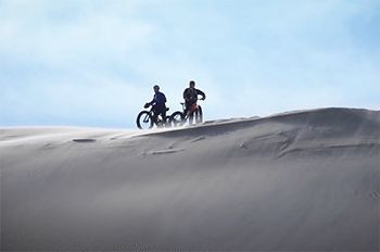 two fat-tire bikers resting on dune ridge