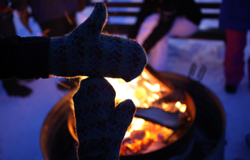 Two mittened hands make the shape of Michigan as a warm campfire blazes in the background.
