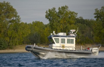 A conservation officer boat cruises past a small, wooded island while on an agitated river.