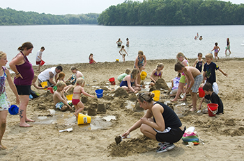 A large group of beachgoers are shown enjoying an afternoon along the shore of an inland lake.