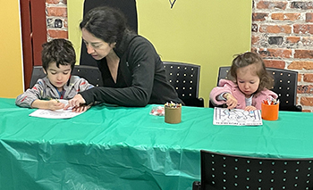 A couple of young children color with the oversight of a woman at the Outdoor Adventure Center.