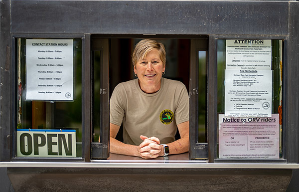 seasonal park worker leaning out contact booth smiling with open sign