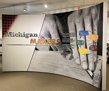 large, curved exhibit panel in mostly sepia tones, with the title Michigan Makers and some text, and overlaid colorful flow chart of questions