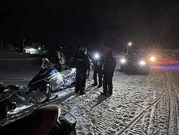 DNR conservation officers are shown contacting snowmobilers at night along a trail.