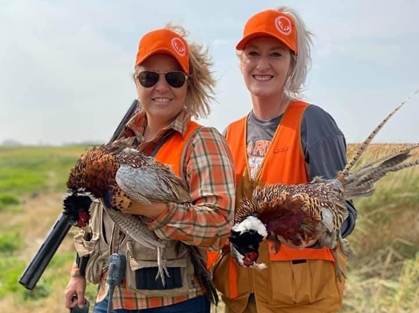 two women in hunting gear holding harvested pheasants