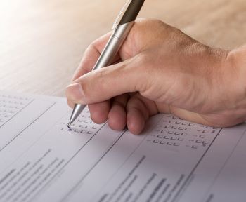 Image of a person's hand holding a pen to fill out a survey