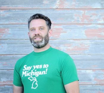Portrait of Justin Knepper. He has short dark hair, a beard, and is wearing a green "Say yes to Michigan!" shirt.
