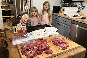 Three young girls in a kitchen with processed meat on table