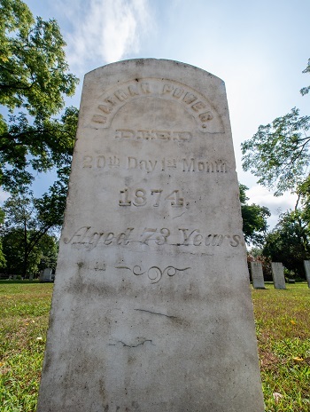 a tall, round-topped, whitewashed headstone, backed by a blue sky and clouds and trees, reads Nathan Parker, died 1874, aged 73