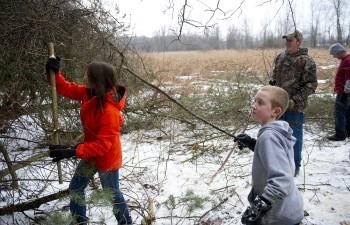 Two children, with two adults supervising, tend to an overgrown area.