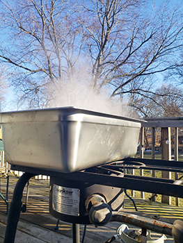A boiler for sap is shown working on an outdoor deck, with steam rising into the air.
