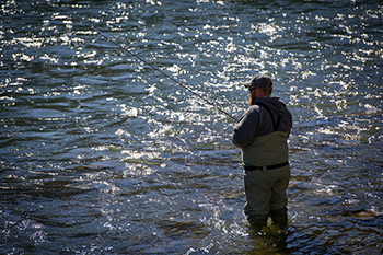 An angler wades in knee-deep water, eyes focused on their bobber in the mildly agitated waves.