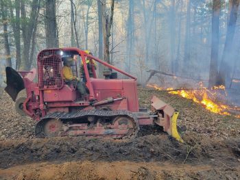 A firefighter drives a bulldozer to create a line of earth intended to stop a fire in its tracks. 