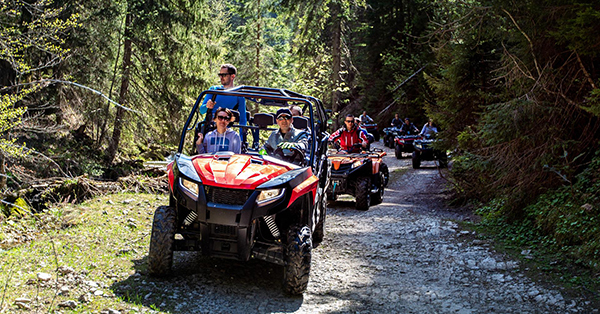 People riding in ORVs on wooded trail