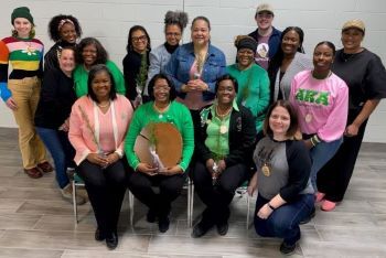 A group of Alpha Kappa Alpha Sorority, Inc. members holding seedlings, with DNR trainers, pose for a photo