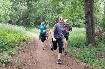 A group of kids run excitedly down a dirt forest path.